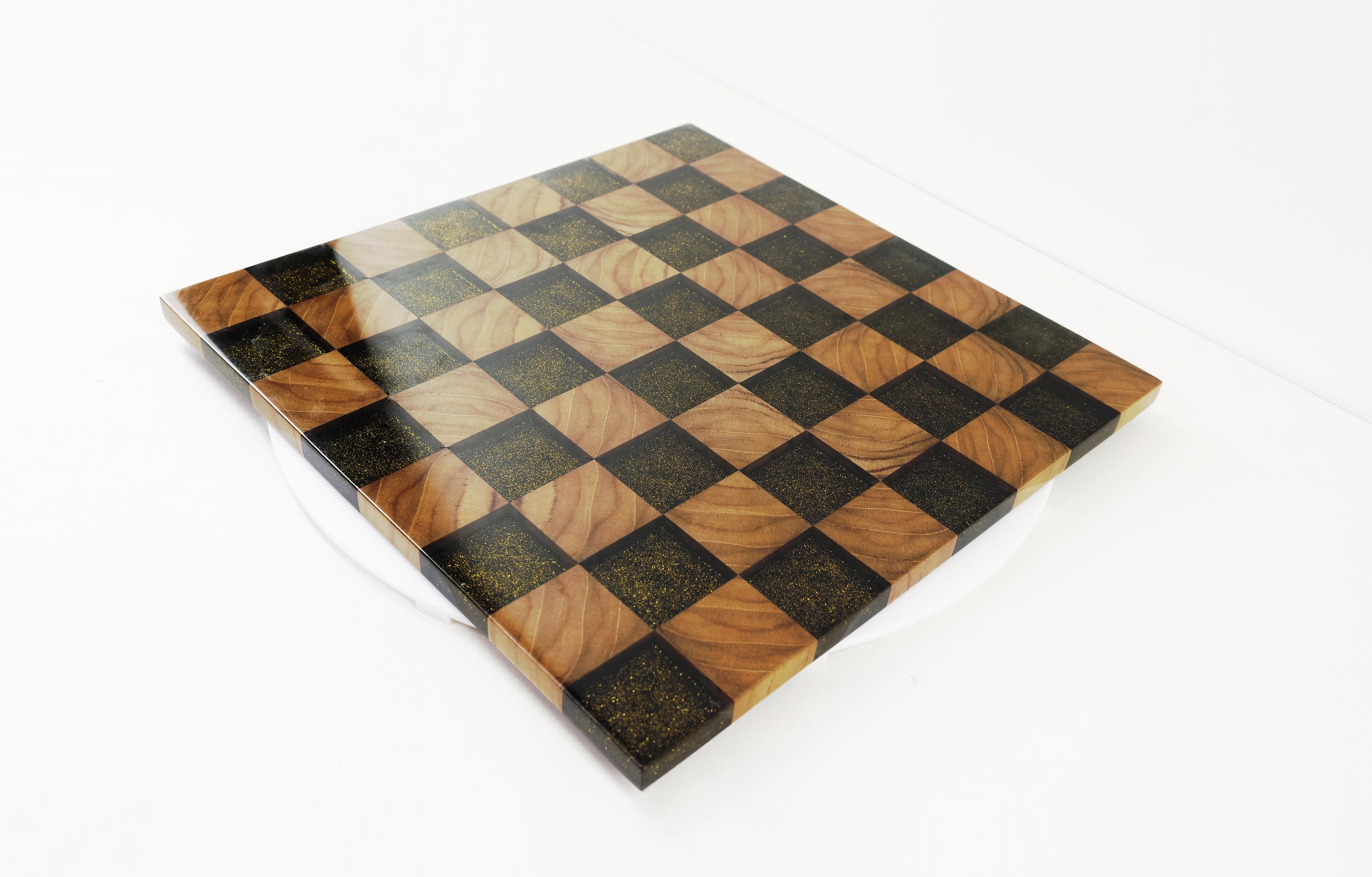 Golden Gambit Schachbrett aus Massivholz und schwarzem Epoxidharz – schräg von vorne fotografiert. Handgefertigtes Designprodukt mit Goldflakes und hochglanzlackierter Oberfläche.
