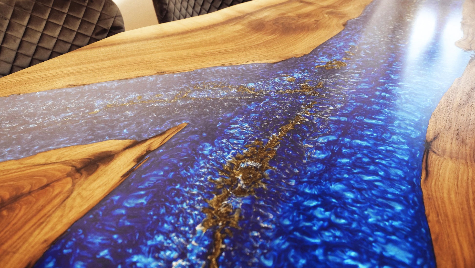 Makroaufnahme des Epoxidharz-Inlays im Blue Ember Esstisch – goldene Pigmente schweben im blauen Harz wie Sternenstaub. Hochwertige Verarbeitung und luxuriöse Materialkomposition.