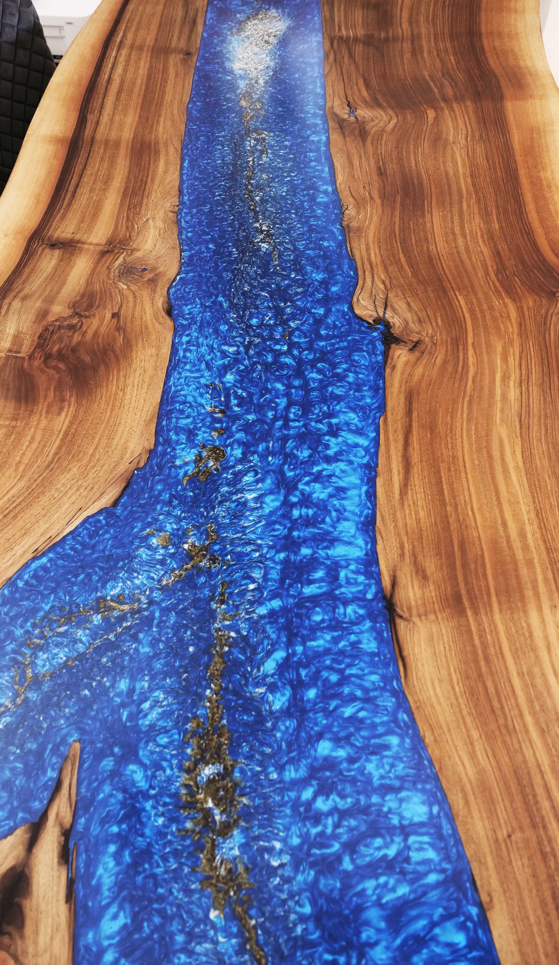 Detailansicht der Tischoberfläche des Blue Ember Esstischs – organisches Blasenbild im tiefblauen Epoxidharz, eingerahmt von lebendiger Nussbaum-Maserung. Einzigartiges Designmöbel mit Seele.