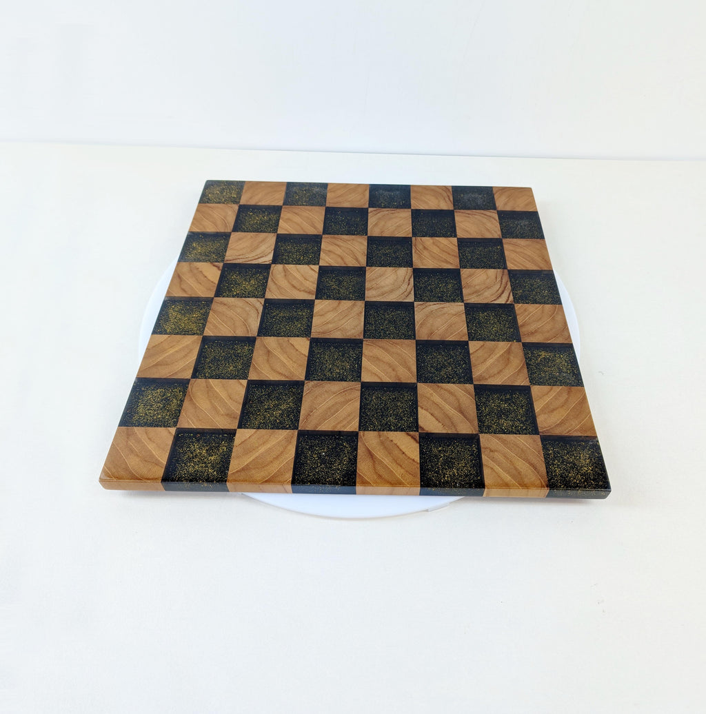 Golden Gambit Design-Schachbrett aus Teakholz und schwarzem Epoxidharz – schräg von der Seite aufgenommen. Detailreiche Verarbeitung, luxuriöse Materialien und strukturierte Oberfläche.