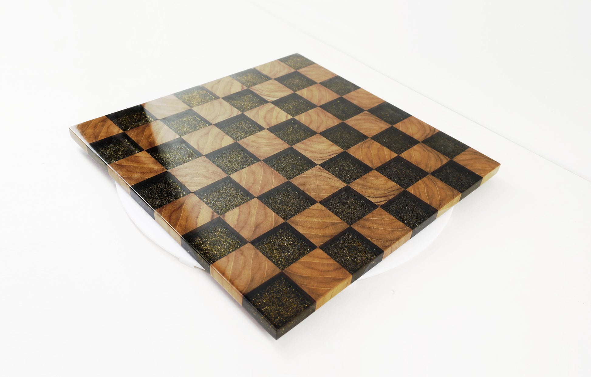Golden Gambit Schachbrett aus Massivholz und schwarzem Epoxidharz – schräg von vorne fotografiert. Handgefertigtes Designprodukt mit Goldflakes und hochglanzlackierter Oberfläche.