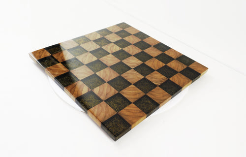 Golden Gambit Schachbrett aus Massivholz und schwarzem Epoxidharz – schräg von vorne fotografiert. Handgefertigtes Designprodukt mit Goldflakes und hochglanzlackierter Oberfläche.