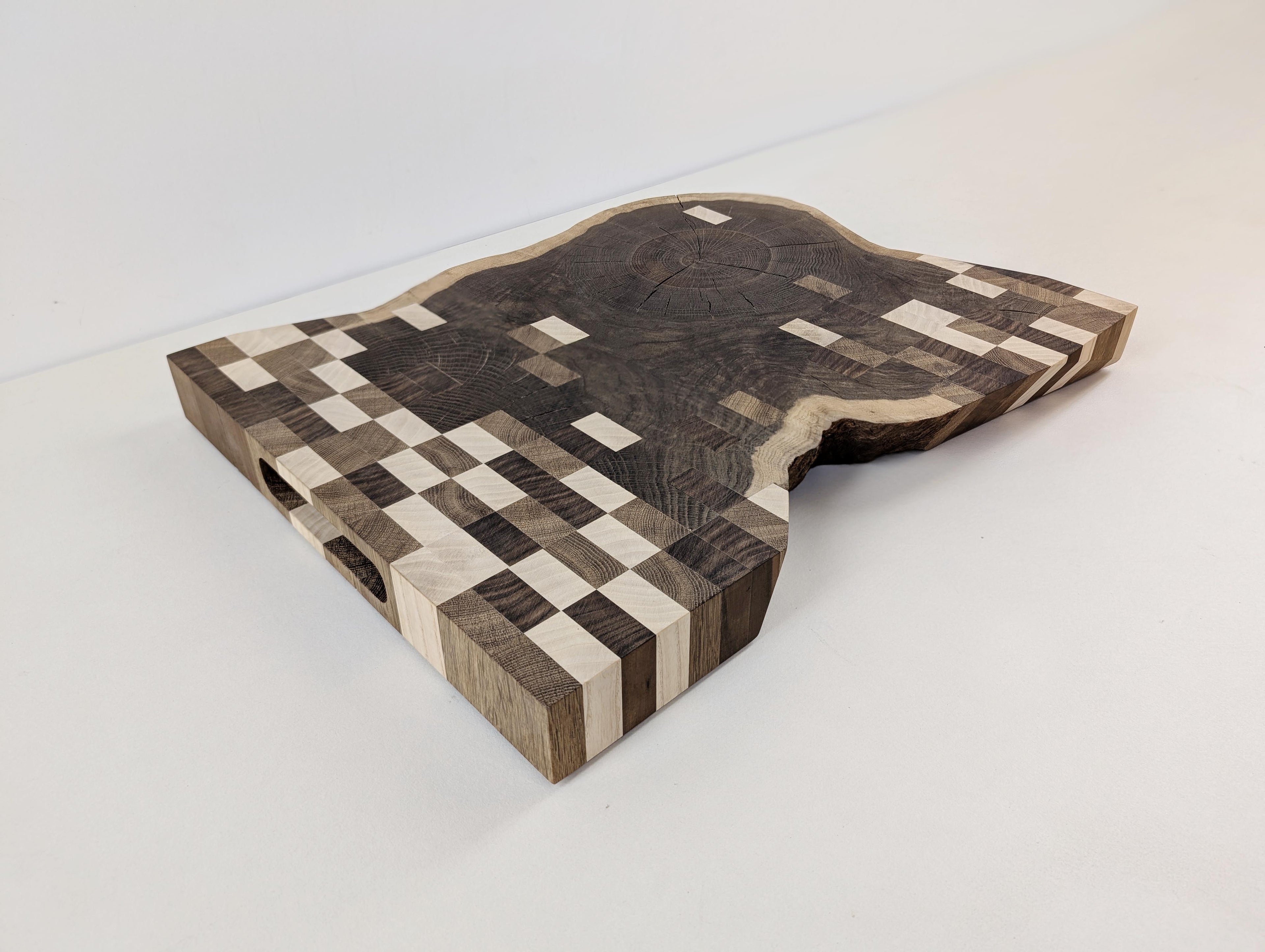 Design-Schneidebrett aus Massivholz – handgefertigt aus Eiche mit Inlays aus Esche und Nussbaum. Einzigartiges Rasterdesign, fotografiert schräg von vorne.