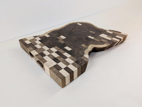 Design-Schneidebrett aus Massivholz – handgefertigt aus Eiche mit Inlays aus Esche und Nussbaum. Einzigartiges Rasterdesign, fotografiert schräg von vorne.