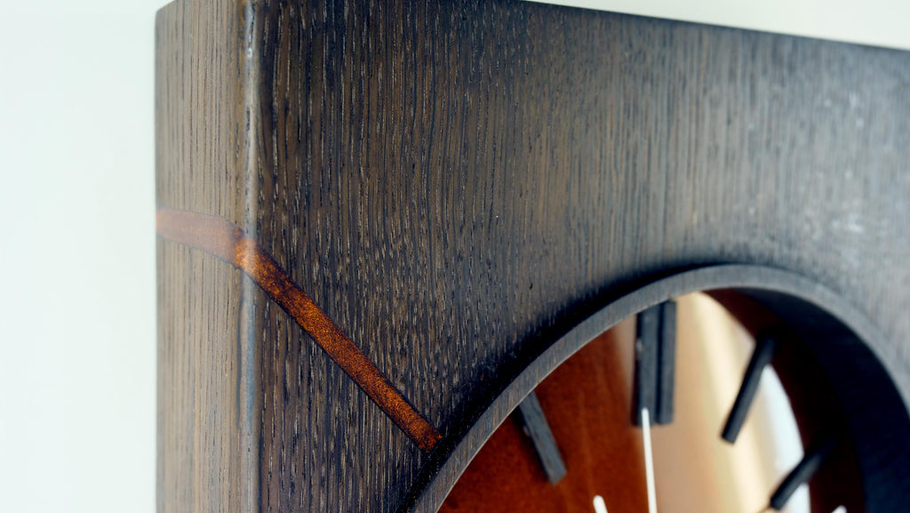 „Detailaufnahme der oberen linken Ecke der Kupferzeit Wanduhr – diagonaler Epoxidharzstreifen mit kupferfarbenem Pigment und markanter Holzmaserung in geräucherter Eiche, Design by Steigerwood