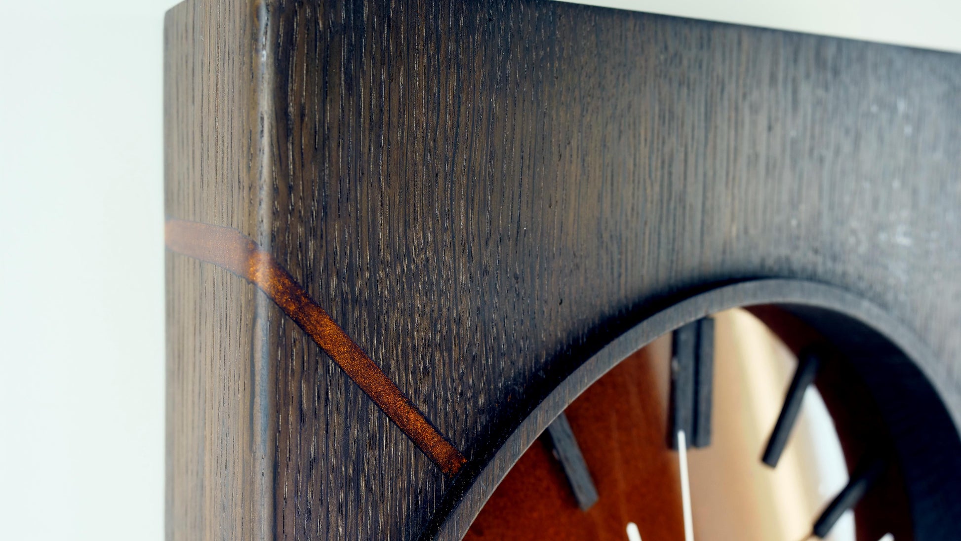 „Detailaufnahme der oberen linken Ecke der Kupferzeit Wanduhr – diagonaler Epoxidharzstreifen mit kupferfarbenem Pigment und markanter Holzmaserung in geräucherter Eiche, Design by Steigerwood